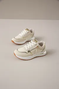 Zapatillas de moda crema con detalles metálicos dorados y cremallera lateral.
