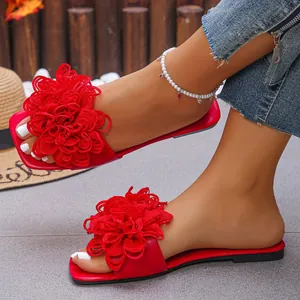 Close-up of red flat sandals featuring a vibrant 3D fabric flower detail on the strap.