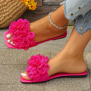 Detail view of fuchsia flat sandals featuring vibrant large fabric flower decorations
