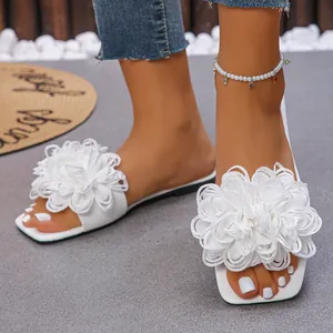 Close-up of white flat sandals featuring large elegant fabric flowers for summer beachwear