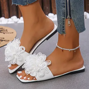 Detail view of elegant white flat slide sandals featuring large 3D fabric flowers.