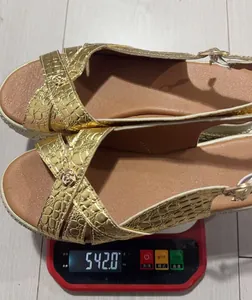 Close-up of women's gold wedge platform sandals being weighed on a digital scale at 542 grams