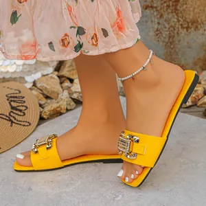 Detalle de sandalias planas amarillas con hebilla dorada decorativa y una tobillera