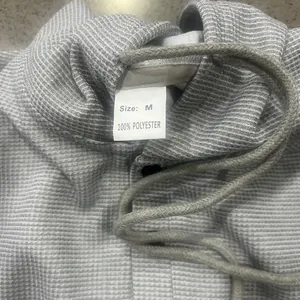 Macro view of gray waffle knit hoodie showing 100% polyester label and drawstring.