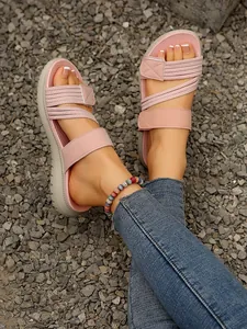Gros plan de sandales compensées roses avec brides croisées et Velcro sur gravier