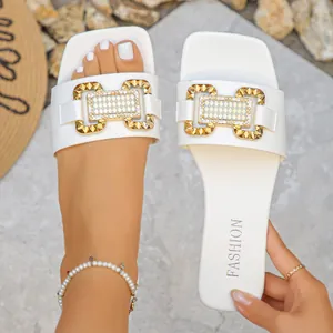 Primer plano de sandalia plana blanca con hebilla dorada decorativa y pedrería para mujer.