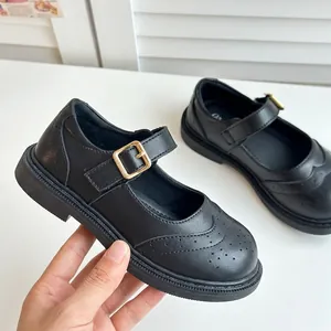 Détail de chaussures Mary Jane noires pour filles avec boucle dorée et perforations.