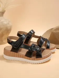 Close-up of black platform wedge sandals for women with bow decoration and white stitching