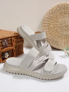 Gros plan de sandales compensées beiges avec brides velcro et détails tressés.