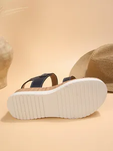 Detailed view of white serrated sole on navy blue wedge sandal with wood texture.