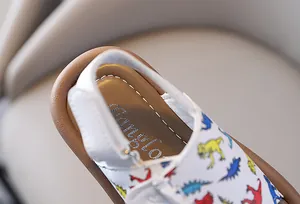 Close-up detail of toddler sandals showing white leather and colorful dinosaur prints