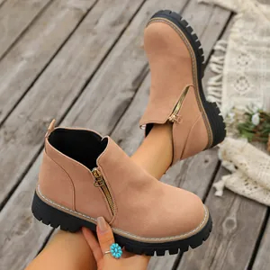 Primer plano de elegantes botines de ante beige con cremallera y suela negra gruesa.