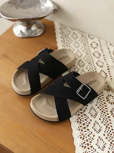 Stilvolle schwarze Sandalen mit Kreuzriemen und Silberschnalle auf einem Holztisch.