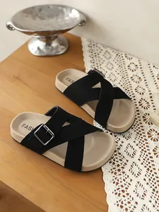 Detailansicht schwarzer Sandalen mit Kreuzriemen und Metallschnallen auf Holzoberfläche