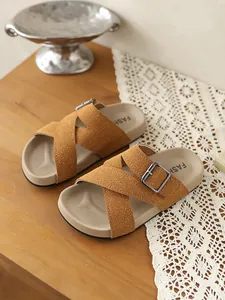 Detailaufnahme von hochwertigen braunen Kreuzriemen-Sandalen mit Metallschnallen auf Holz