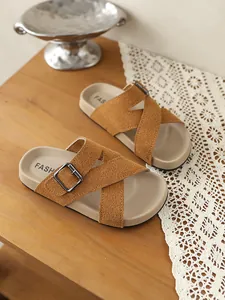 Nahaufnahme von braunen Vintage-Sandalen mit Kreuzriemen und Schnalle auf Holztisch.