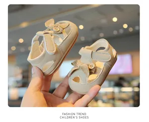 Close-up of beige baby closed-toe sandals featuring elegant bow and button decorations.