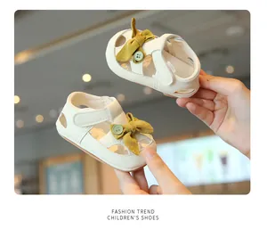 Close-up of cream baby walking sandals with yellow bow and button detail