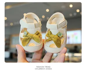 Close-up of cream baby girl walking sandals with mustard yellow bow detail