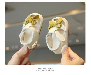 Close-up of off-white baby girl princess sandals with mustard yellow bow and velcro