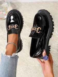 Λεπτομερής προβολή των μαύρων λουστρίνι loafers με πλατφόρμα και χρυσή αλυσίδα