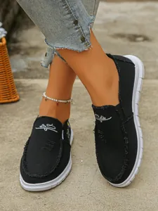 Detail view of comfortable black canvas slip-on shoes with frayed edges and thick white soles