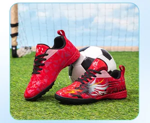 Close-up of red children's turf soccer shoes with flame pattern on artificial grass