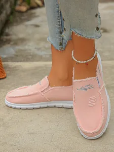 Close-up detail of stylish pink canvas slip-on loafers with frayed edge and white sole.