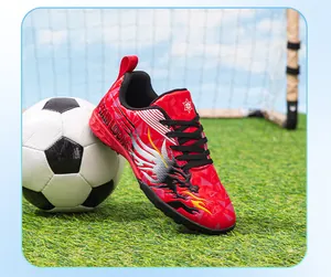 Close-up of red children's soccer shoe with dragon design on grass next to ball
