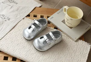 Zapatos Mary Jane plateados brillantes para niñas con hebillas sobre fondo beige