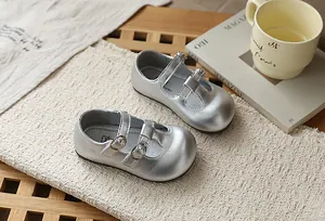 Detalle de zapatos Mary Jane plateados para niña con diseño calado y correa de hebilla