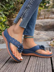 Stijlvolle blauwe sleehak teenslippers met bloemen en klinknagels op een houten terras