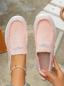 Detailed view of pink canvas slip-on loafers with frayed edges and embroidery.