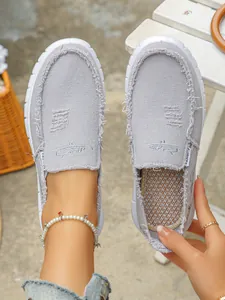Close-up of grey canvas slip-on loafers with frayed edges and embroidered details
