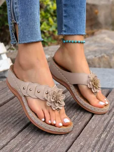 Close-up van beige teenslippers met sleehak, grote bloemdecoratie en metalen studs
