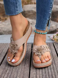 Detailopname van beige sleehak teenslippers met decoratieve bloemen en klinknagels