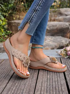 Detail van dames sleehak slippers met bloemen en klinknagels op houten terras