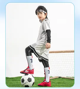 Detailed view of red children's TF soccer shoes on grass with a soccer ball