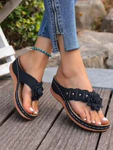 Close-up van zwarte sleehak slippers met bloem- en klinknageldetails gedragen aan de voet.