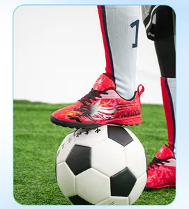 Close-up of red kids turf soccer shoes with dragon design on artificial grass soccer ball