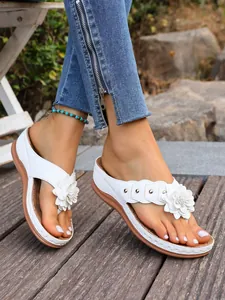 Detail van witte sleehak teenslippers met delicate bloemaccenten en metalen klinknagels