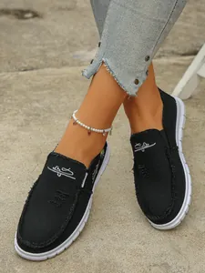 A detailed view showing stylish black canvas loafers with frayed edges and embroidery
