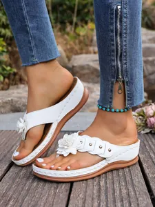 Detailopname van witte sleehak teenslippers met decoratieve bloemen op een houten terras