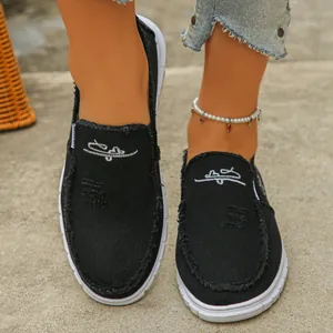 Close-up of black canvas slip-on shoes featuring white embroidery details and frayed edges