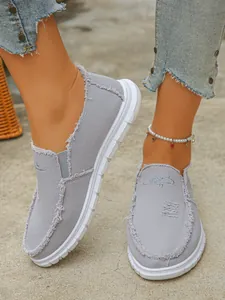 Detailed view of stylish grey frayed canvas slip-on loafers for women shown on feet