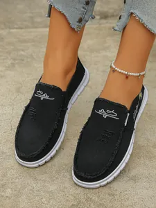 Close-up of women's black canvas slip-on shoes with frayed edges and embroidery