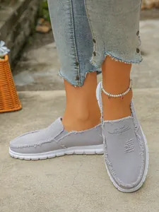Close-up of stylish grey canvas slip-on loafers with frayed edges and pearl anklet