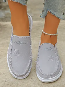 Close-up view of women's light purple canvas slip-on loafers with stylish frayed edges on feet