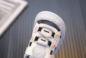 Macro view of white children's sandals showing stitching and cute orange paw print patterns