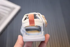 Detailed back view of a toddler white soft sole sandal featuring an orange heel pull tab